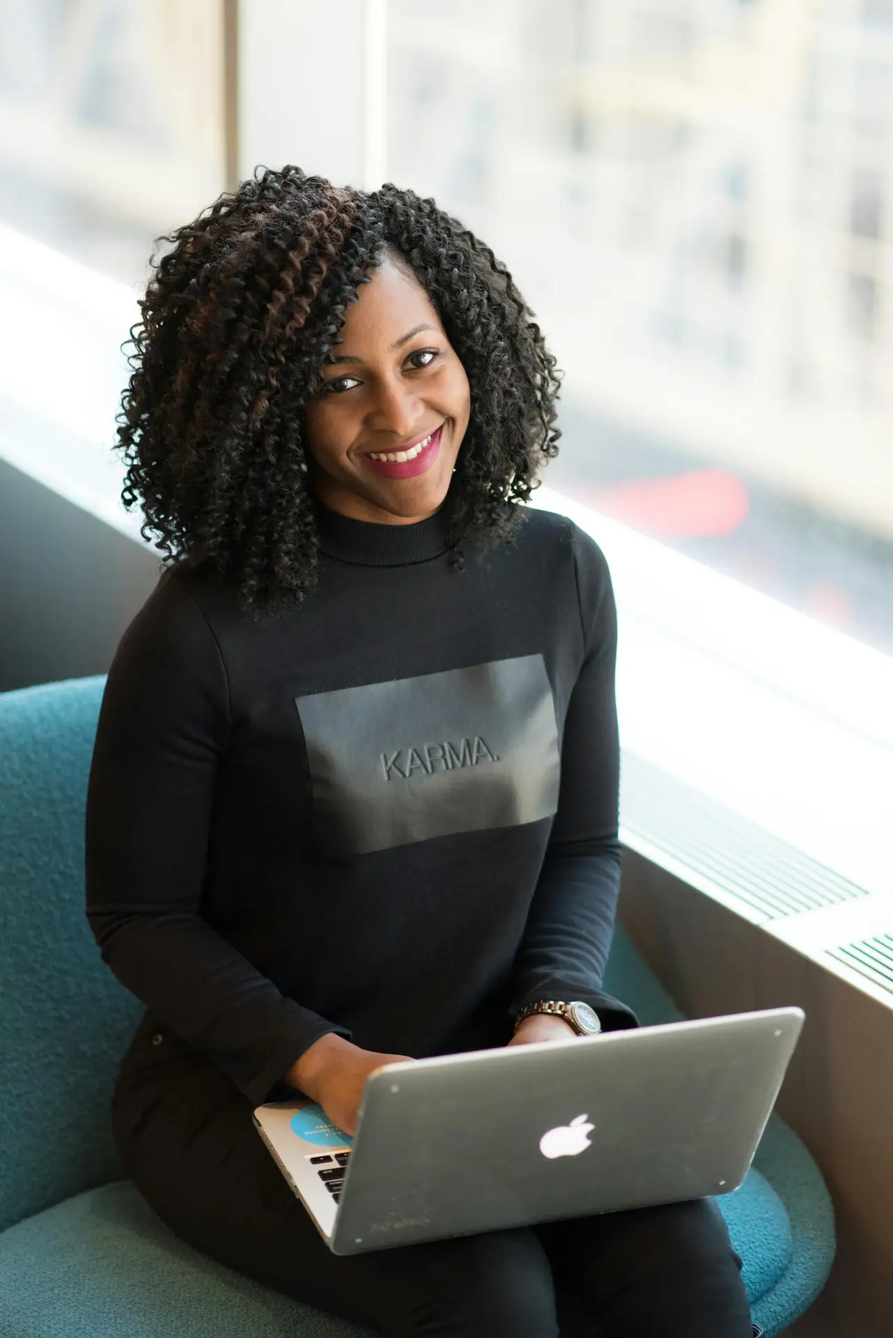 Beautiful African American woman with curly hair smiling while using a laptop indoors.