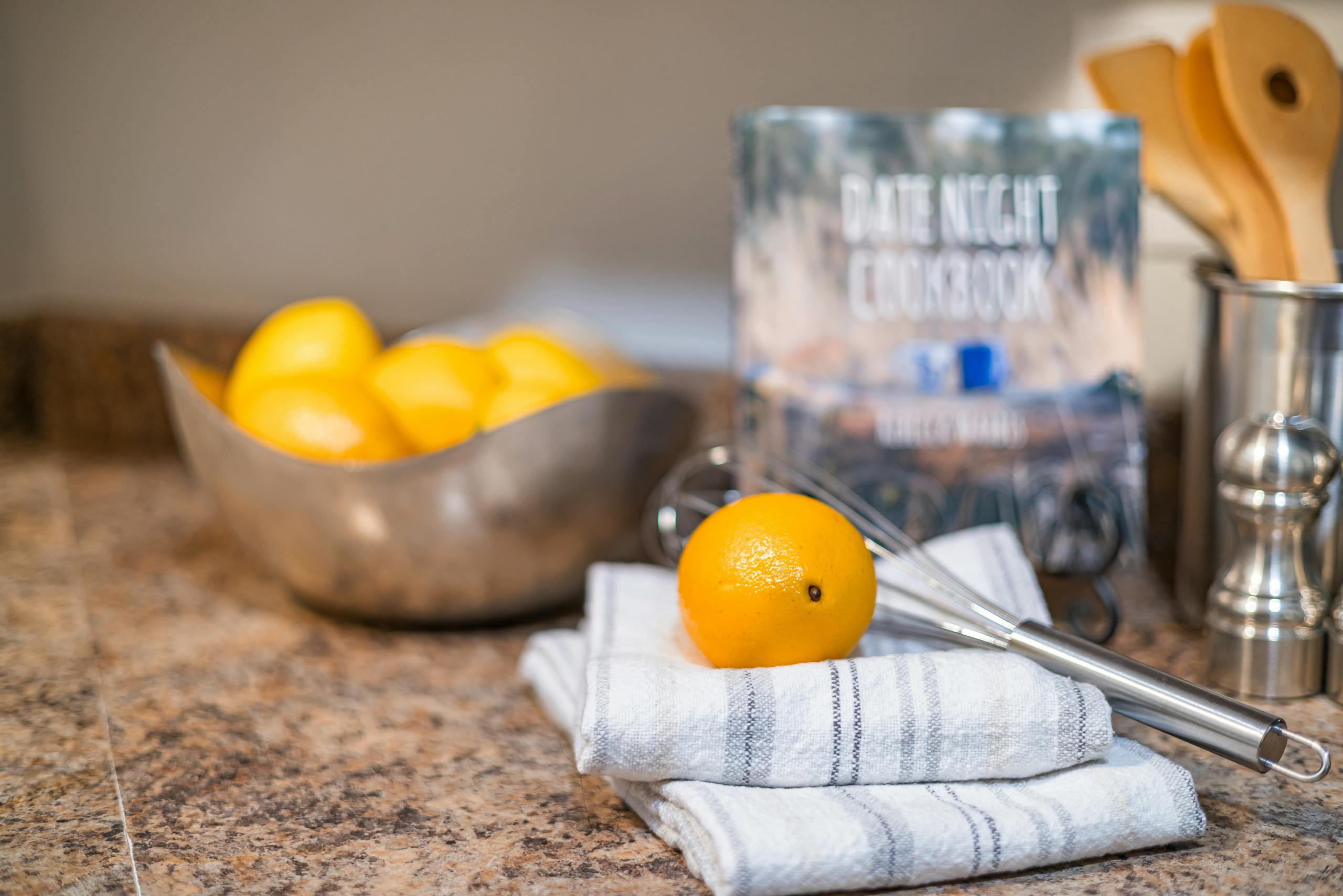 A warm kitchen scene featuring lemons, utensils, and a cook book on a countertop.